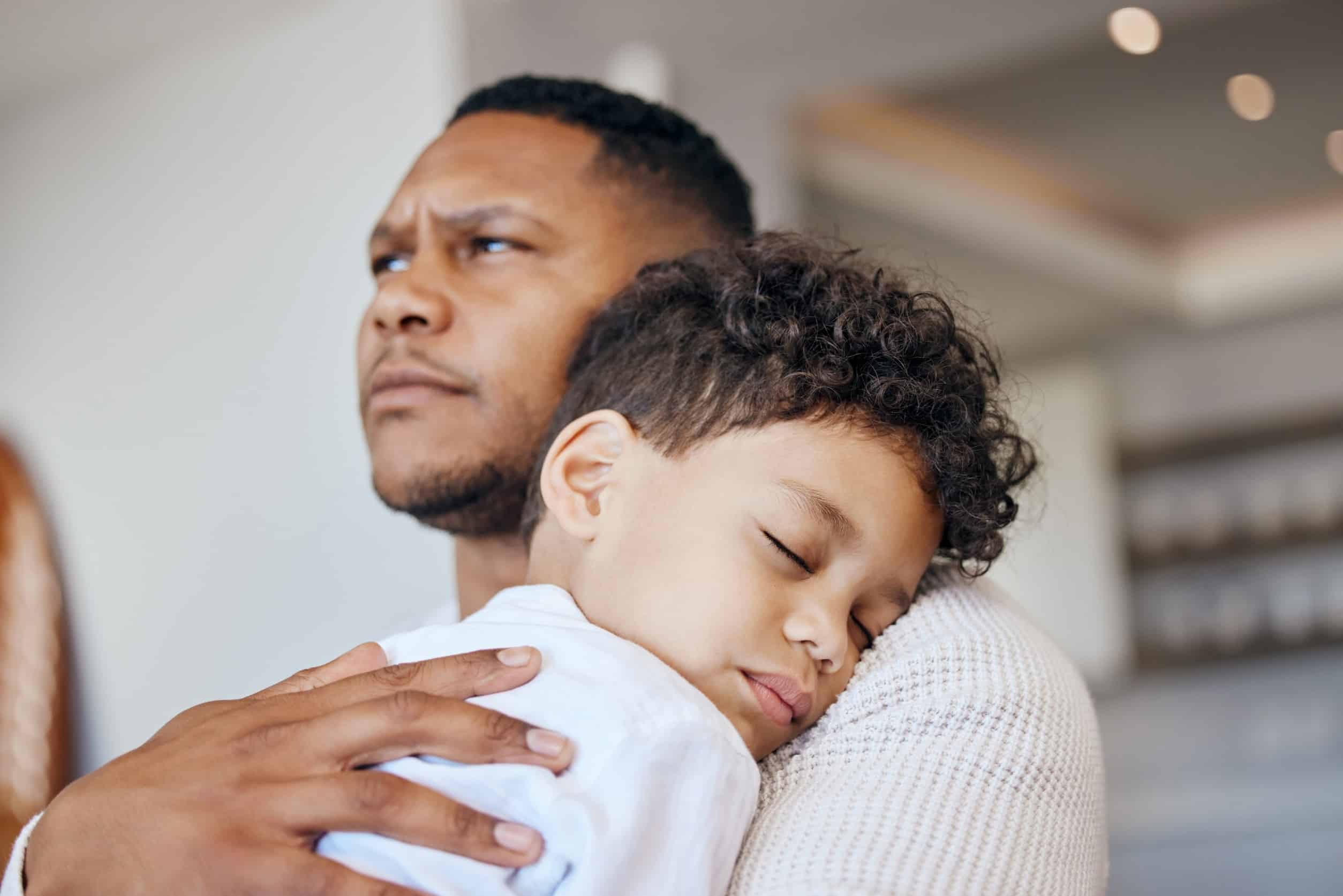 A father with his son sleeping on his shoulder.