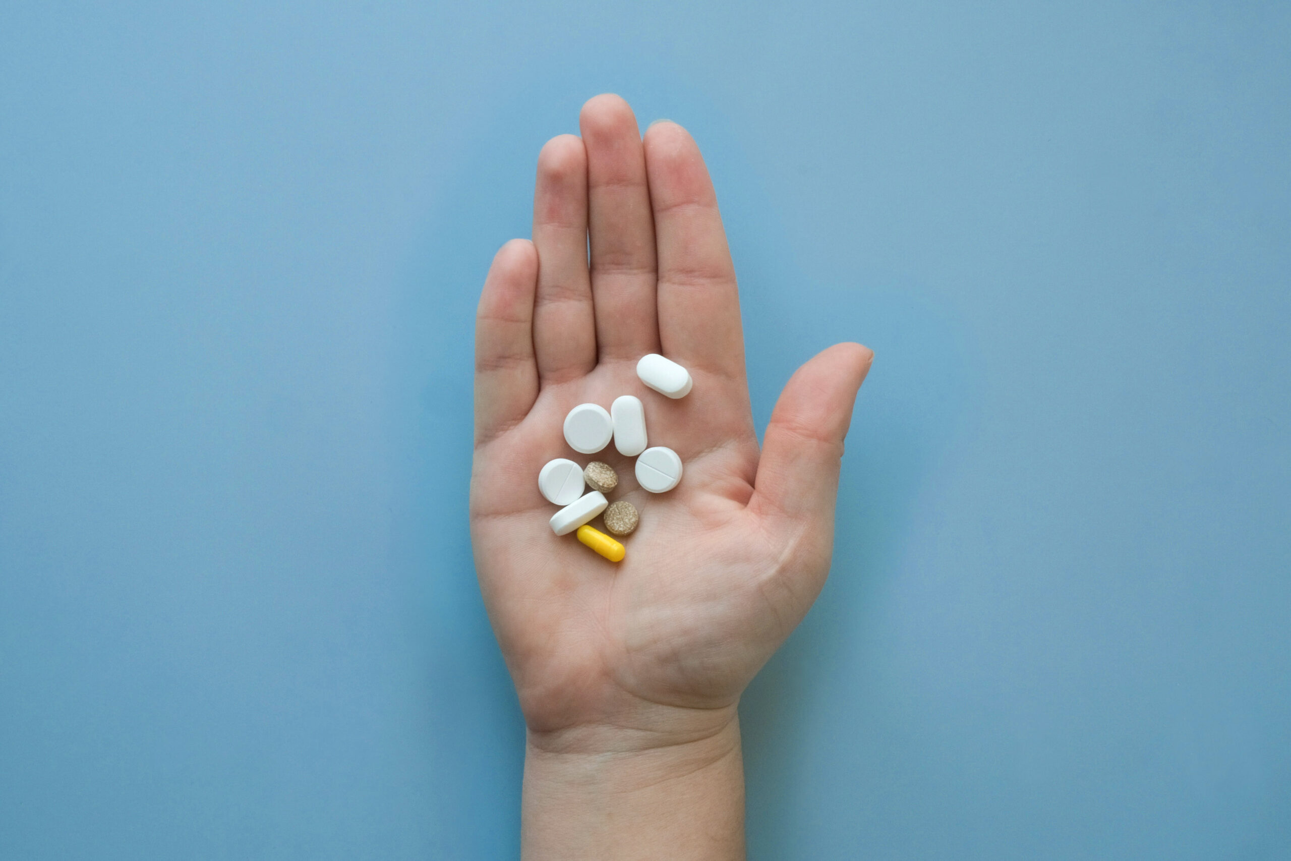 open hand holding array of pills over blue background